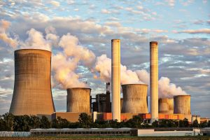 Power plant emitting smoke from large cooling towers, illustrating the environmental impact of high energy consumption and the importance of green IT practices to reduce carbon emissions.