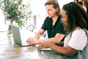 Two colleagues collaborating on a laptop in a bright, green-inspired workspace, symbolizing teamwork in sustainable software development and green IT practices.