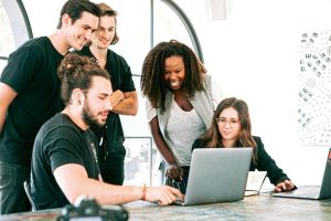 A group of diverse colleagues gathered around a laptop, collaborating and discussing ideas, symbolizing teamwork in green IT and sustainable software development.