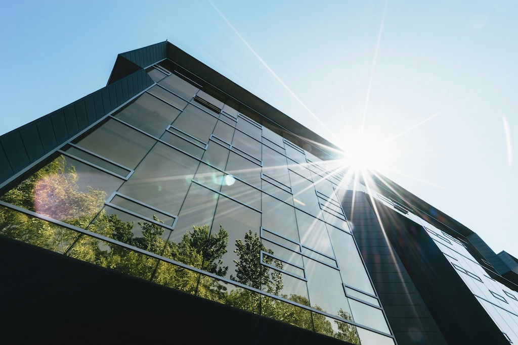 A modern building with reflective glass windows, showcasing greenery and sunlight, symbolizing sustainable architecture and the integration of eco-friendly Green IT practices within corporate infrastructure.