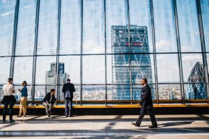 Image of a man walking inside an office building with the view of another office building outside.